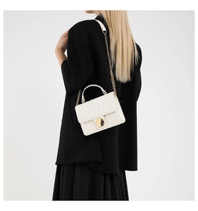 Detailed view of white quilted bag with gold hardware worn over a black blazer