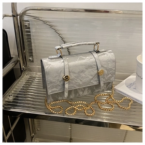 Macro detail of silver pleated faux leather texture and gold chain on handbag