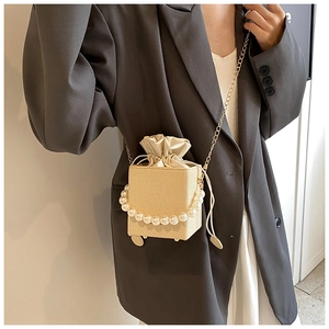 Detail of woven beige texture and elegant pearl beads on a crossbody bag with chain strap