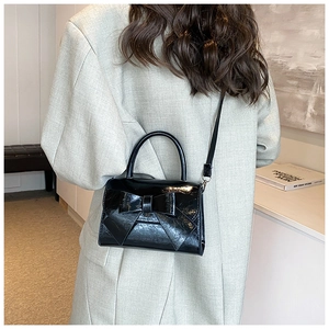 Model view of black patent leather handbag with bow detail and adjustable shoulder strap