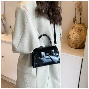 Detail of black patent leather crossbody bag featuring a large bow and top handle