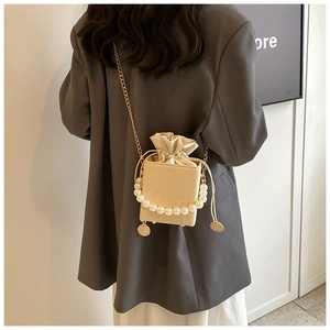 Détail d'un mini sac seau tissé beige avec poignée en perles et bandoulière dorée