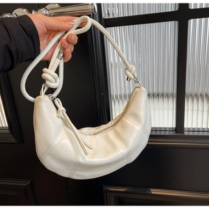 Detail view of white croissant shoulder bag featuring knotted strap and stitched leather