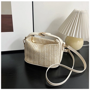 Detail of woven straw crossbody bag with beige leather trim and gold metal clasp
