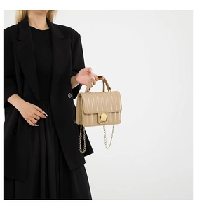 Detail of light beige quilted handbag featuring large gold circular buckle and metal chain