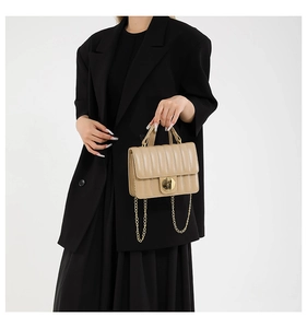 Detail of beige quilted flap handbag with gold metal lock and chain strap on a black outfit