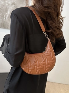 Brown half-moon shoulder bag with geometric embossing and adjustable strap on a model