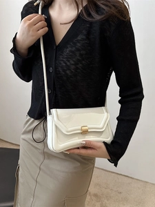 Minimalist white patent leather saddle bag with gold buckle worn by model