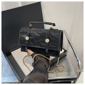 Detail of black pleated texture handbag with golden chain strap and round buckles