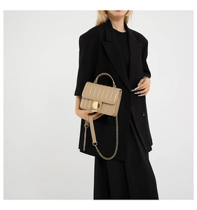 Detail of beige quilted handbag with gold circular metal buckle and chain strap