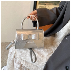 Silver metallic handbag with large bow detail and round top handle on model