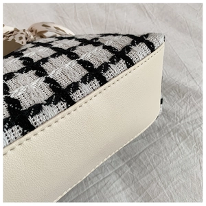 Detail of tweed tote bag showing houndstooth texture, leather trim and beige stitching