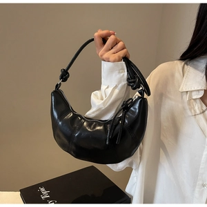 Close-up of black croissant shoulder bag with knotted strap and waxy leather texture