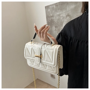 Detail of white quilted crossbody bag with golden metal clasp and chain strap
