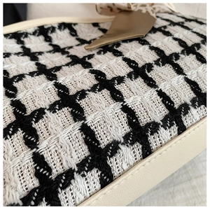 Close-up of black and white tweed texture with cream leather trim and satin ribbon