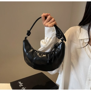 Close-up of black croissant bag with unique knotted strap and silver zipper detail