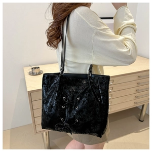 Close-up of a glossy black leather tote bag featuring detailed lace-up bow design