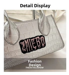 Detail of silver crocodile pattern handbag with ZMIEBO embroidered logo patch