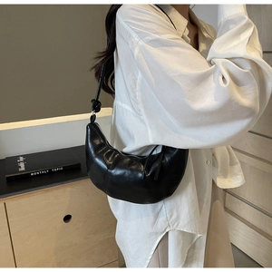 Detail of black crescent shoulder bag with knotted strap and silver zipper on white shirt