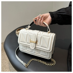 Close-up of white quilted handbag with gold hardware and chain strap on a stand