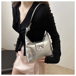 Détail d'un sac sous le bras argenté avec texture froissée brillante et nœud décoratif
