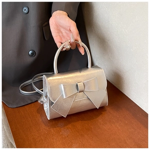 Detail of silver metallic bow handbag showing smooth texture and rounded top handle