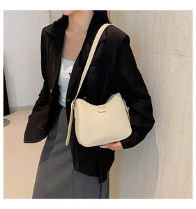 Detail of beige leather underarm bag with gold metal fashion logo on a black blazer