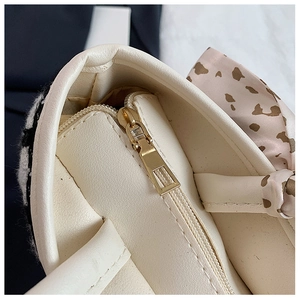 Detail of golden zipper and decorative silk scarf on cream white leather tote bag