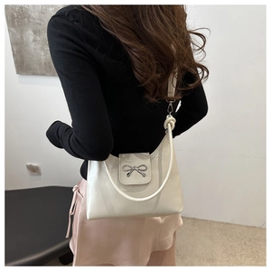 Vue arrière d'un sac d'épaule blanc en cuir verni avec nœud argenté sur mannequin