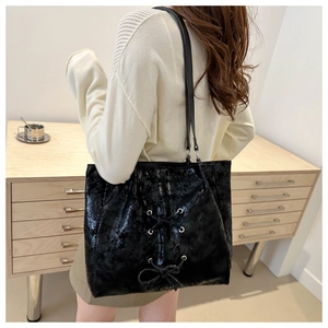 Detail of black bow tote bag showing glossy wrinkled texture and lace-up ribbon design