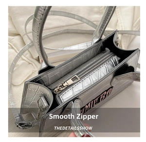 Macro view of silver crocodile embossed texture and smooth metal zipper on square handbag