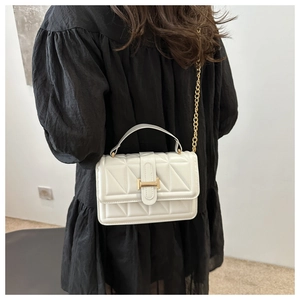 Detailed view of white quilted crossbody bag with gold chain strap on model dress