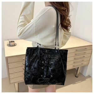 Lifestyle view of a black tote bag with bow detail and textured finish on a shoulder