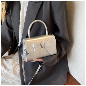 Detail of silver metallic handbag with large bow decoration and curved handle