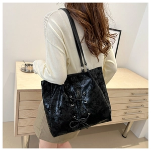 Detail of black leather tote bag with lace-up bow design worn over the shoulder