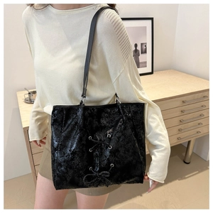 Detail of black glossy faux leather tote bag with silver eyelets and bow tie ribbon accent