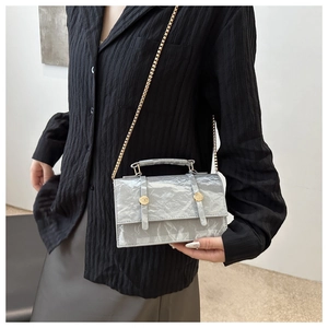 Détail du sac bandoulière gris plissé avec chaîne dorée porté sur une chemise noire