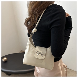 Détail d'un sac à bandoulière crème avec nœud en métal argenté et design de sangle nouée