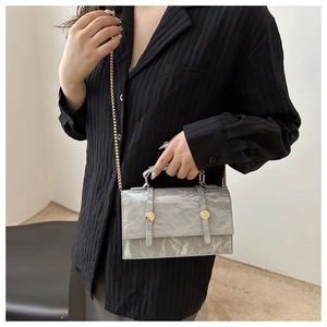 Detail of silver metallic crossbody bag with gold chain strap on a model outfit