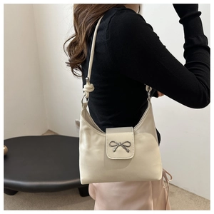 Detail of cream shoulder bag featuring silver bow hardware and knotted strap on model