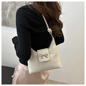 Close-up of beige shoulder bag featuring silver metal bow and knot strap details