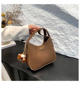 Detail of a brown leather bucket bag with a fashion plaque and plush bear charm
