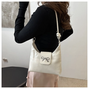 Detail of cream shoulder bag with silver bow accent and stylish knotted strap design