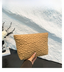 Detail of khaki clutch bag featuring quilted floral texture on lightweight fabric