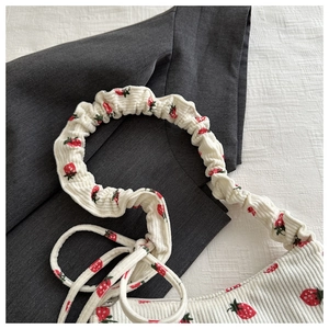 Detail shot of white corduroy shoulder bag featuring red strawberry prints and ruffled strap