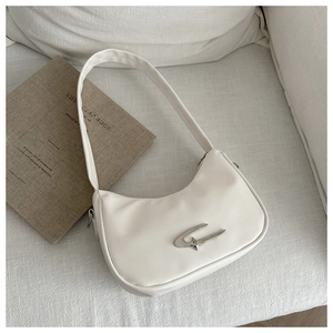 Detailansicht der cremefarbenen Halbmond-Tasche mit silbernem Stern-Logo auf dem Sofa
