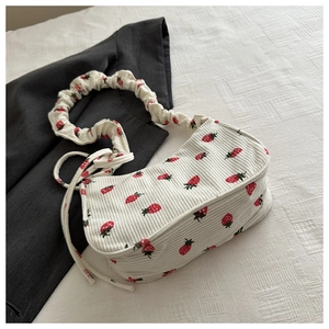 Detailed flat-lay of white corduroy strawberry print baguette bag with scrunchie strap
