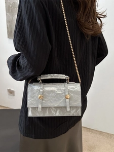 Chic silver pleated crossbody bag with gold hardware and chain strap on a model