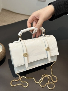 White fashion shoulder bag with glossy wrinkle texture and gold chain strap in hand