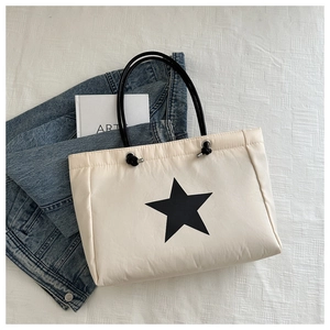 Detail of cream tote bag with black star pattern on a textured white surface